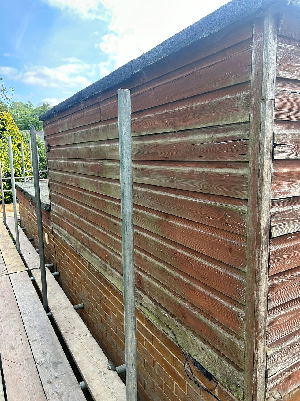 Weathered wooden garden shed with brick base, metal posts alongside, sunny day
