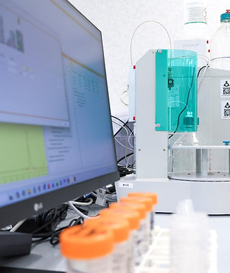 Laboratory benchtop analyzer with reagent bottles beside a computer monitor and sample tubes
