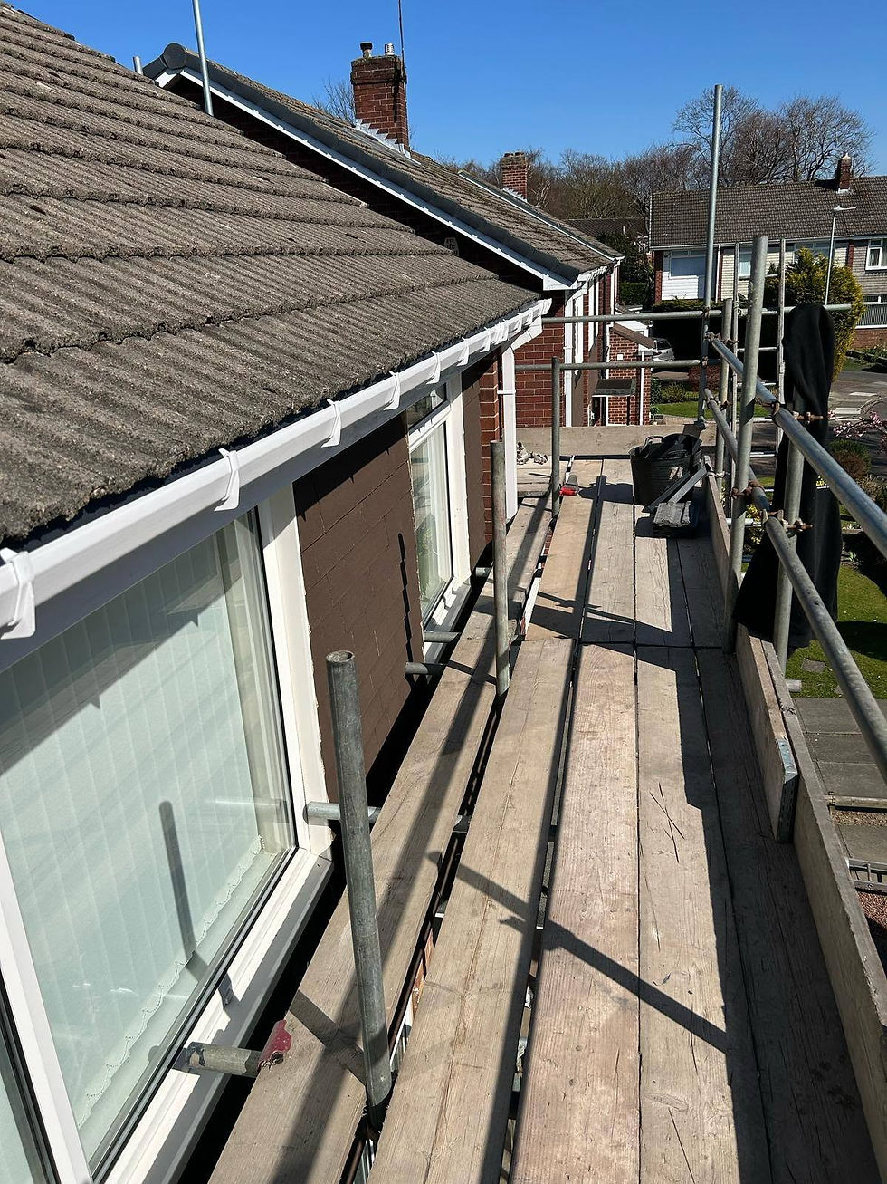 Scaffolding alongside a brick house with new white guttering being installed