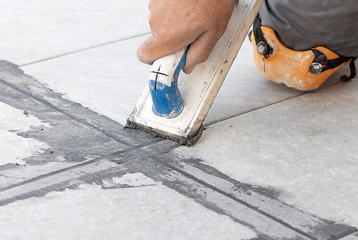 Worker applying grout between floor tiles using a rubber float tool
