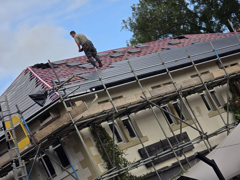 Worker laying dark roof tiles on a building surrounded by scaffolding