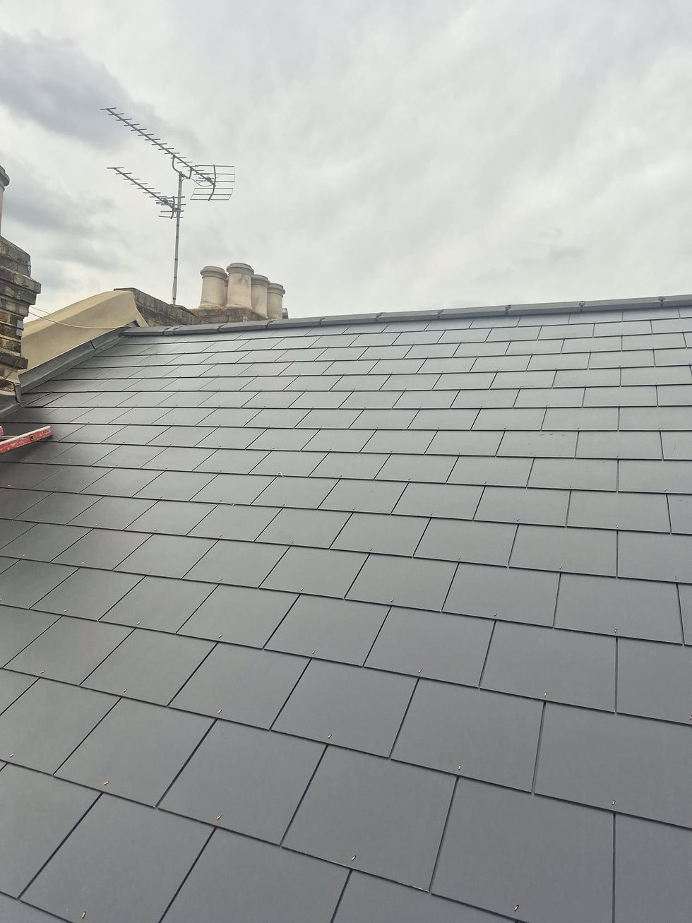 Newly laid grey slate roof with chimney pots and TV aerial beyond