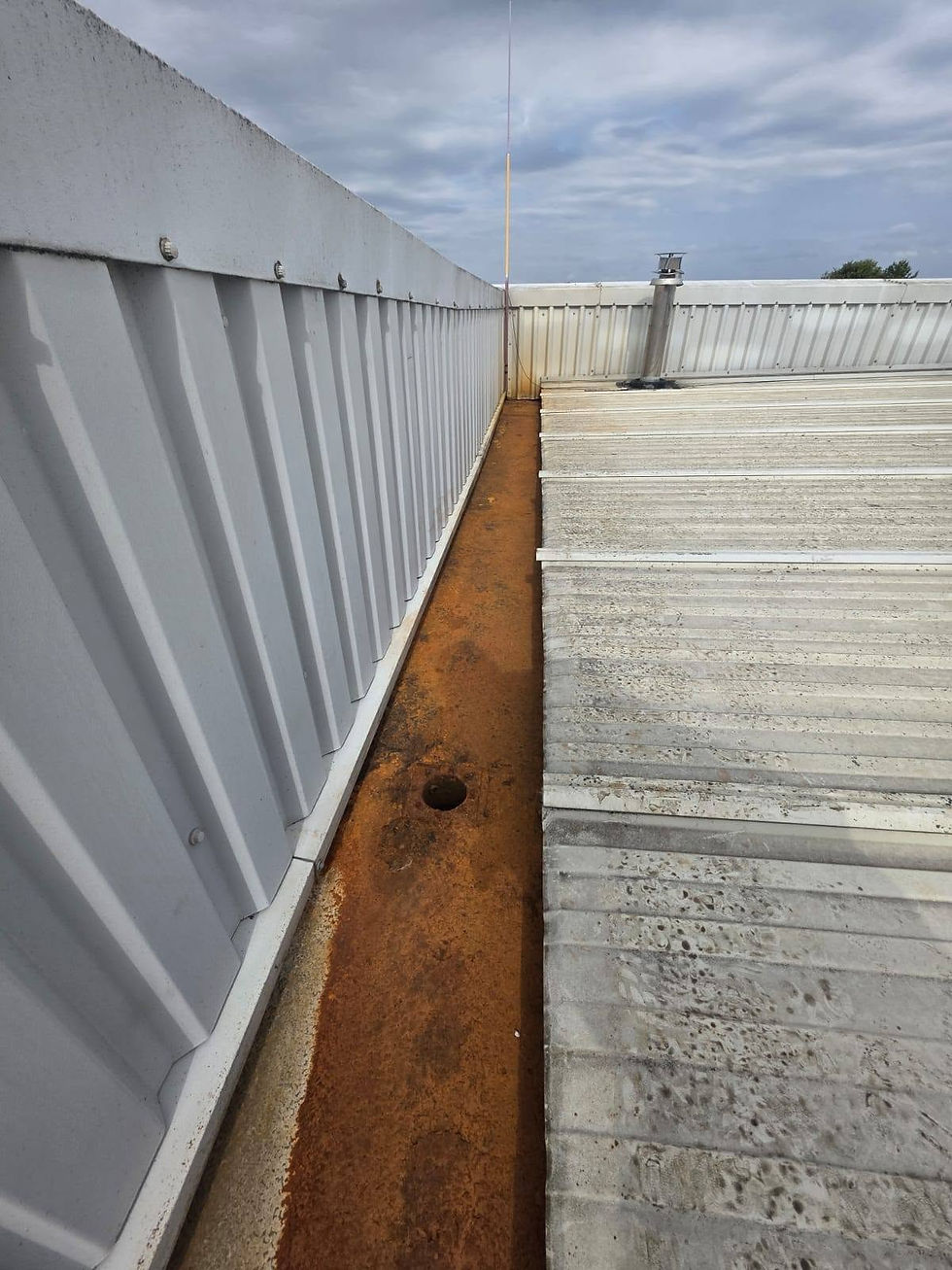 Heavily rusted roof gutter running along a corrugated metal building parapet