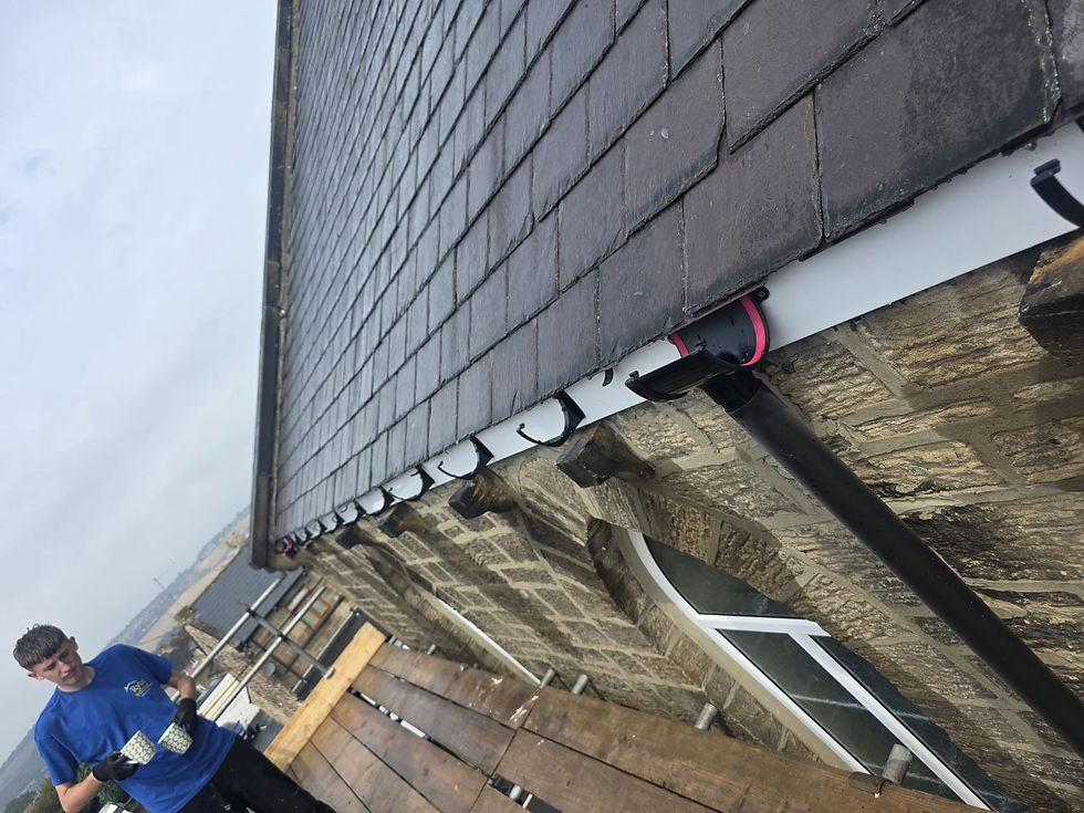 Worker installing black guttering along the eave of a slate-roofed stone building