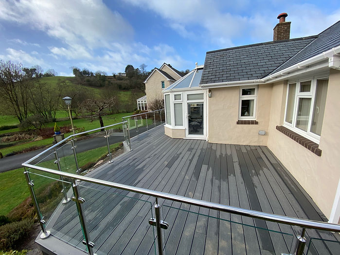 Grey composite deck with glass and steel balustrade beside a bungalow overlooking green hills