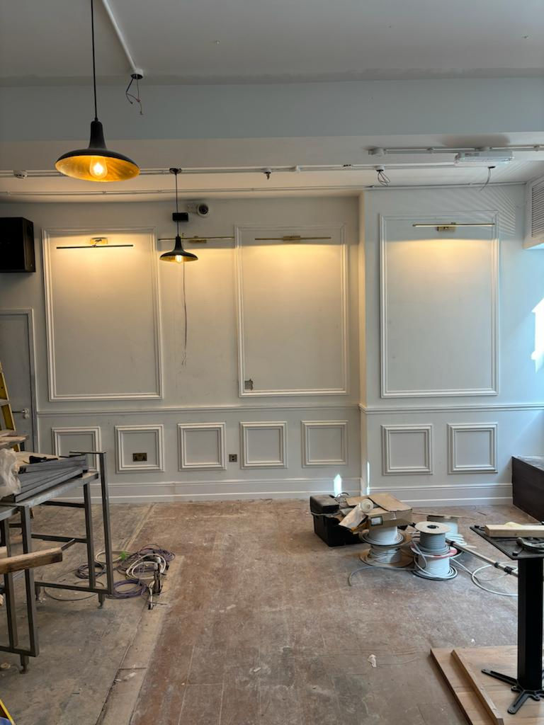 Room under renovation with white paneled walls and paint supplies on floor