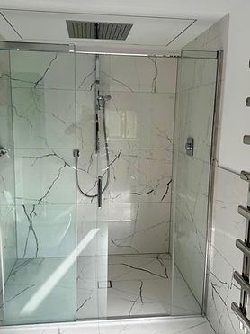 Walk-in glass shower enclosure with marble tiles and chrome heated towel rail
