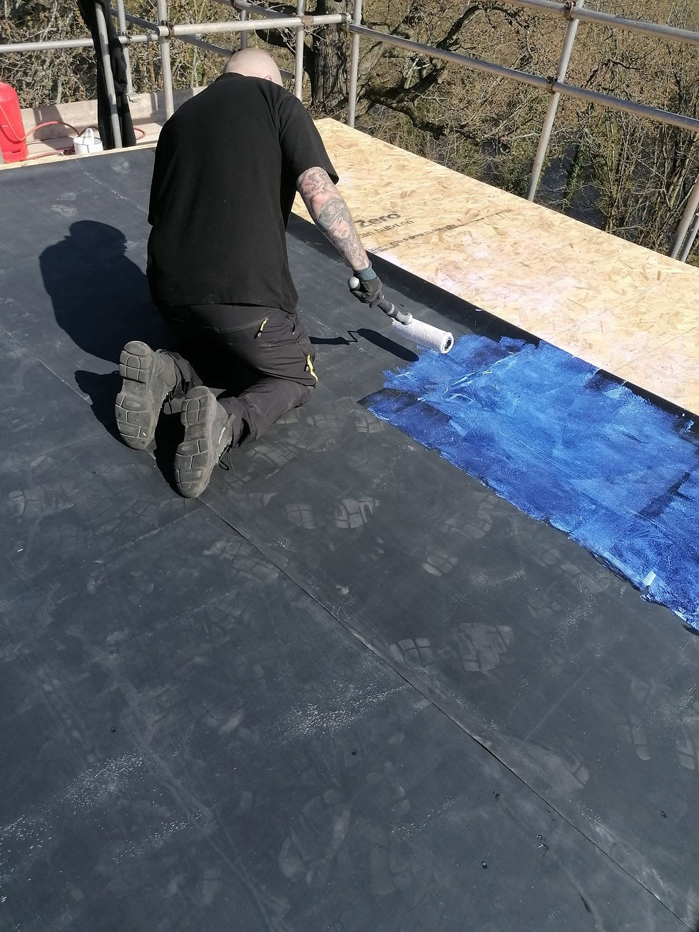 Worker applying blue waterproofing primer to a flat roof with a roller