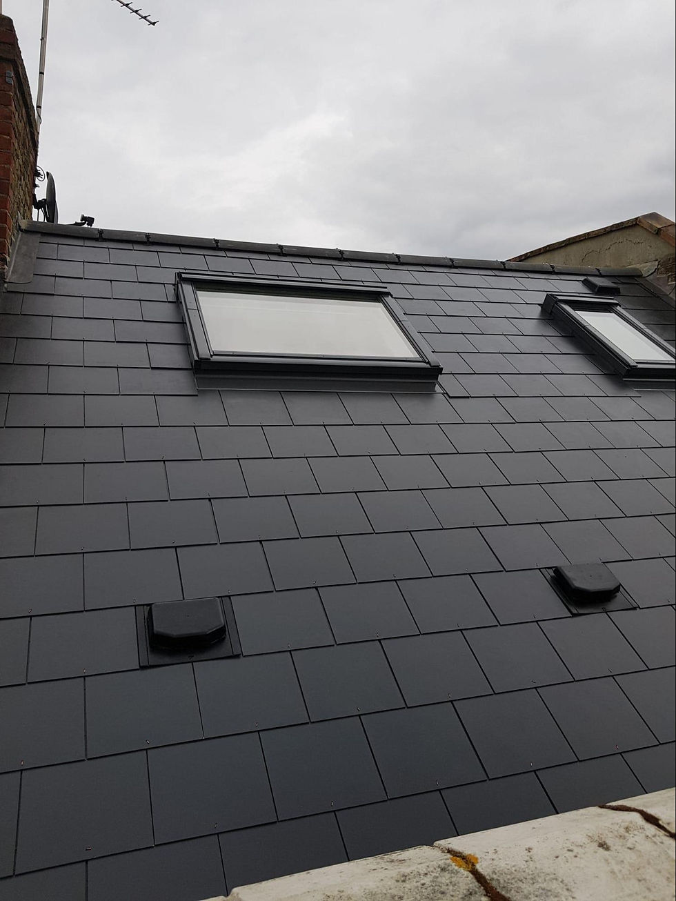 Dark slate roof with two skylights and vent pipes on a residential building