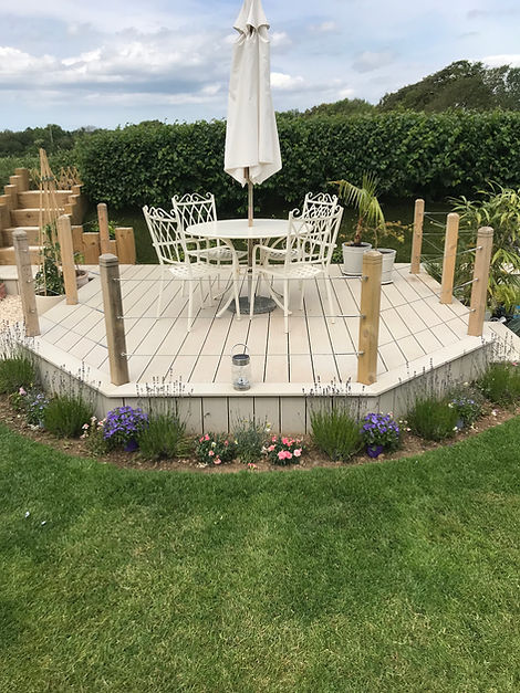 Raised garden deck with white wrought iron table, chairs, and closed parasol, surrounded by lavender and flowers