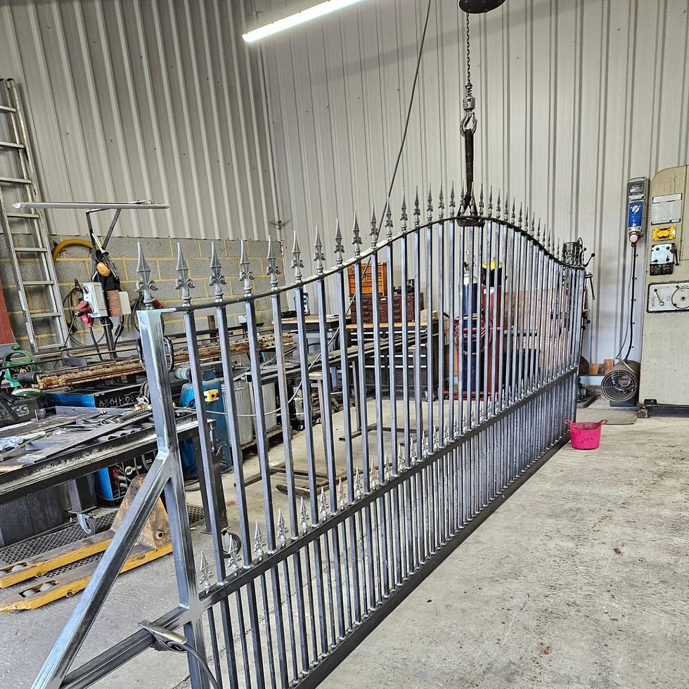 Large ornate wrought iron gate with spear finials inside a metalwork workshop