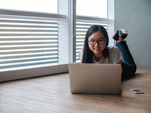 A girl lying on the floor smiling as she looks into a laptop