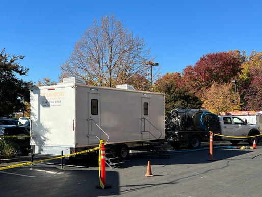 Portable restroom trailer set up in a parking lot beside a service truck and safety cones.