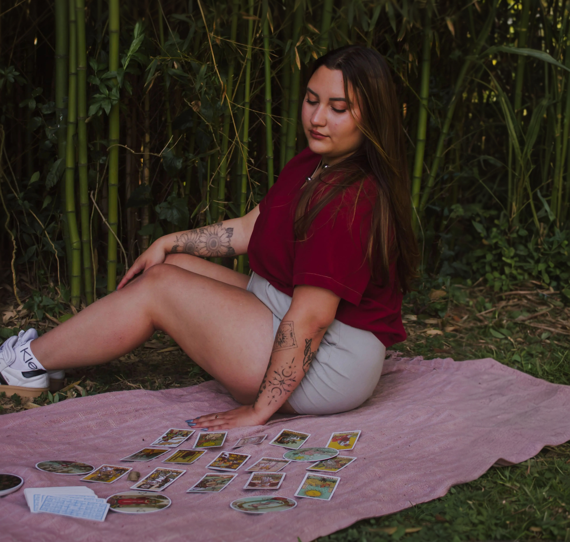 Tarologa Mile sentada ao ar livre, em meio à vegetação, realizando uma leitura de tarot com diversas cartas dispostas sobre um tecido rosa.