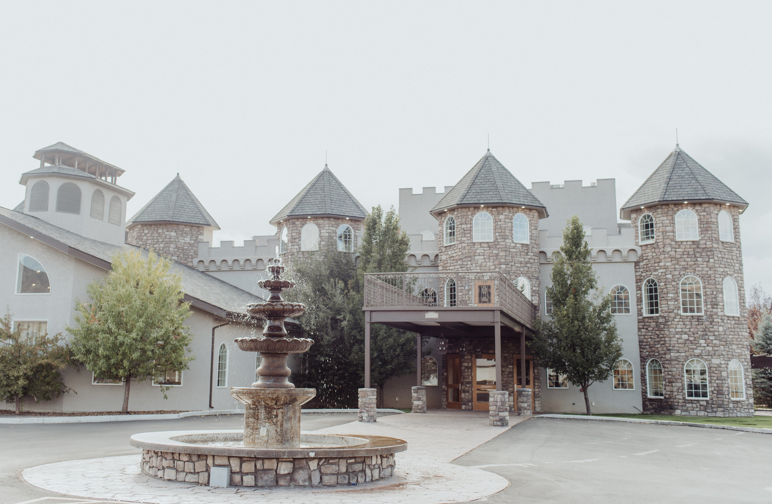 Castle Manor's stone-turreted building in Hyde Park, Utah, with a three-tiered stone fountain in the foreground and a covered stone entrance with wooden double doors