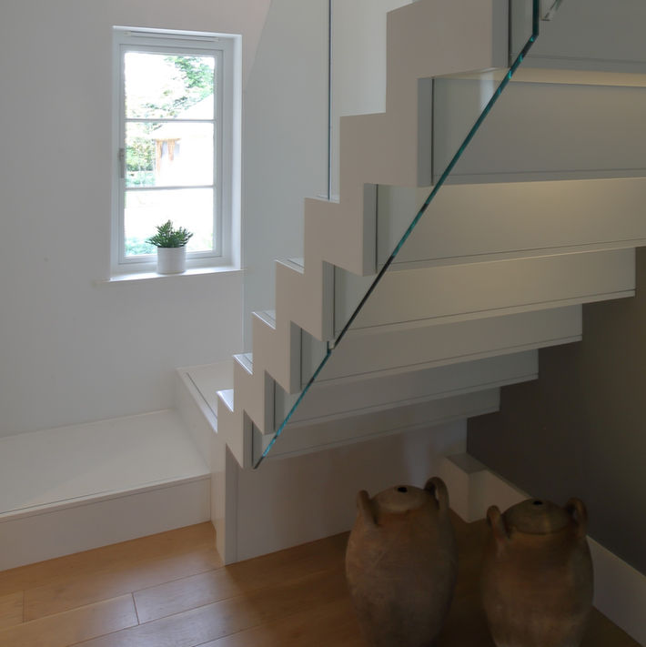 Side detail of bespoke white stair, window in front of stair end with small plant in a pot on the windowsill and two large terracotta pots under the stairs, timber flooring