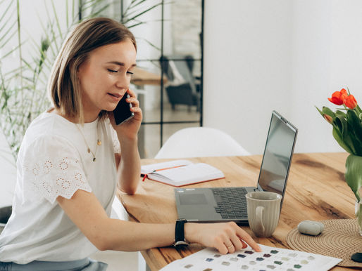 Eine Frau am Tisch mit Laptop und Handy am Ohr