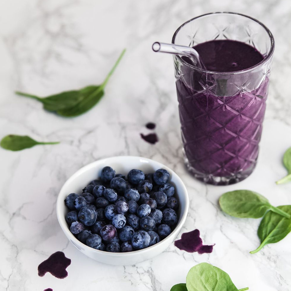 A blueberry and spinach smoothie with a bowl of blueberries and spinach on a granite counter.