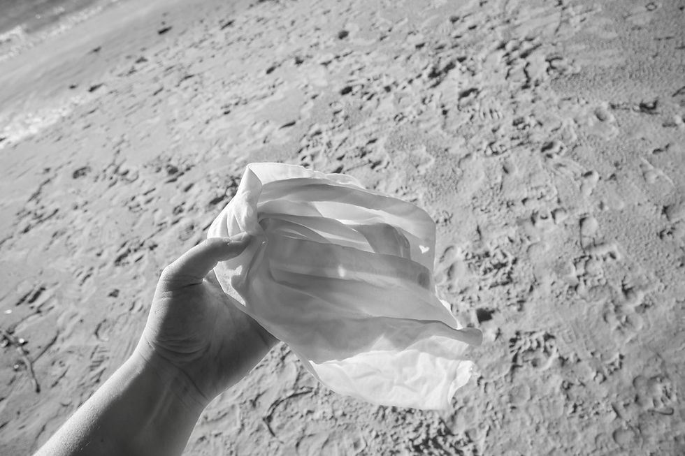 A black and white photograph taken by textile artist and photographer Megan Kennedy of the artist holding a portion of luminous cloth before the camera. There is a coastal landscape in the background.