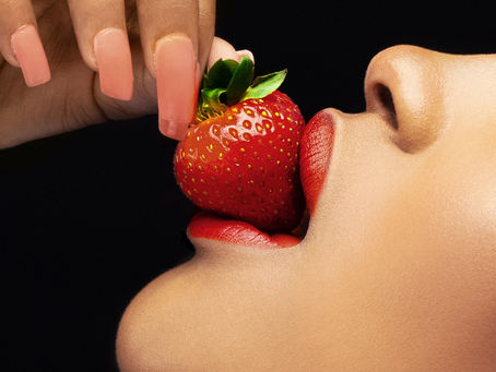 A woman's lips delicately embrace a ripe strawberry, highlighting the vibrant red hue against her smooth complexion.