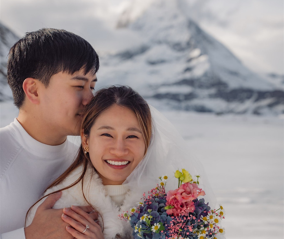 a young couple smiles in all white in the snow for their surprise proposal photos