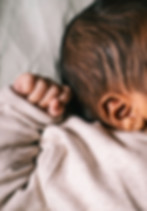 The side of a baby's head as it curls its small hand into a fist