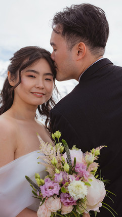 a groom kisses the forehead of his bride who serenely smiles in the snowy alps