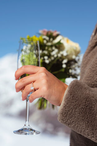 a woman's hand with a new diamond ring on it holding a glass of bubbles and a bouquet of flowers