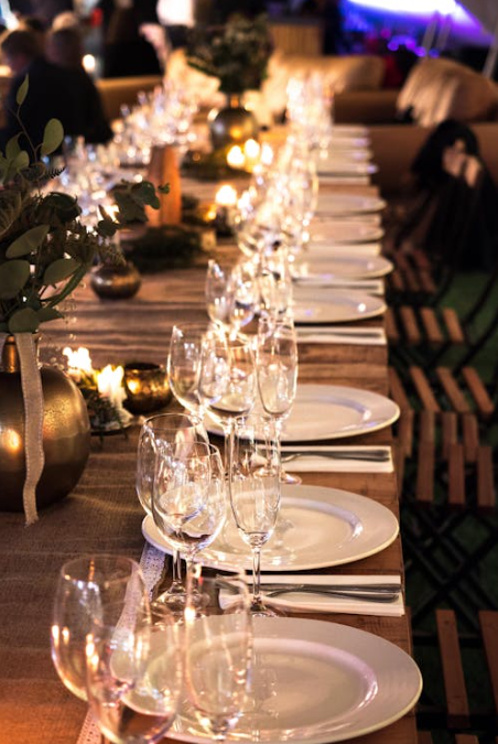 Elegant table set for a dinner party with white plates, glassware, candles, and potted plants. Warm, inviting atmosphere.
