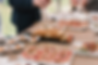 Assorted appetizers on a wooden table, including skewered sandwiches and small dishes. People in formal attire hold champagne glasses.