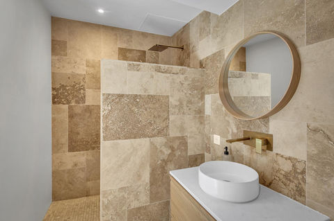 Salle de bain avec vasque blanche, miroir rond et murs en pierre beige.