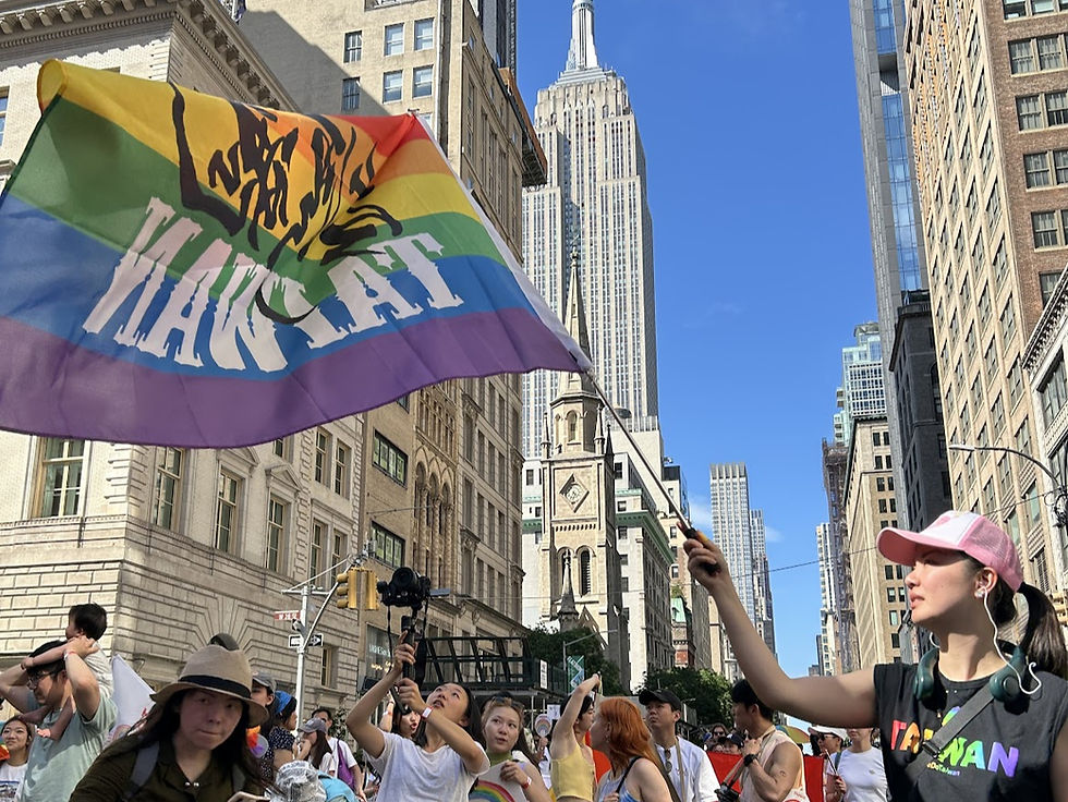 Vickie Wang, a Taiwanese woman, waves a rainbow flag reading "Taiwan Soul" in a New York City Pride parade. The Empire State Building is visible in the background. Crowd is festive.