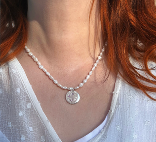 person wearing cream pearl necklace with large silver moon charm