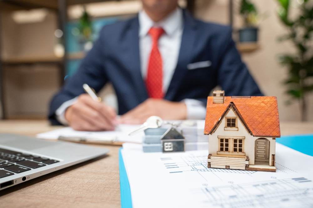 Asesoría inmobiliaria con documentos y una maqueta de vivienda