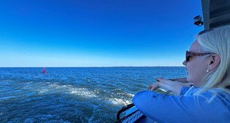 a female tour guide looks relaxed in the sunshine standing at the bow of a boat and staring out to sea.