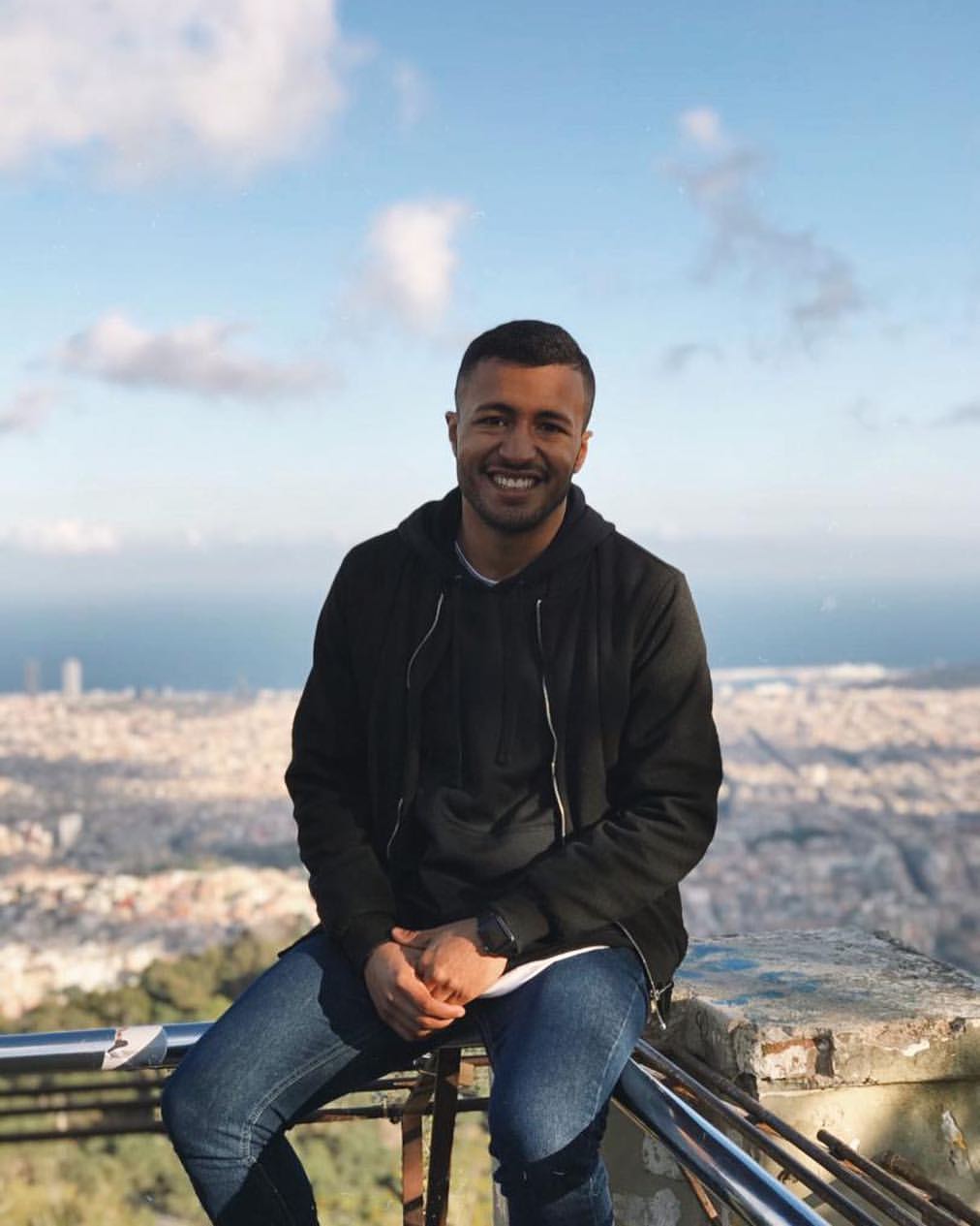 Hombre sonriente sentado con una ciudad costera de fondo
