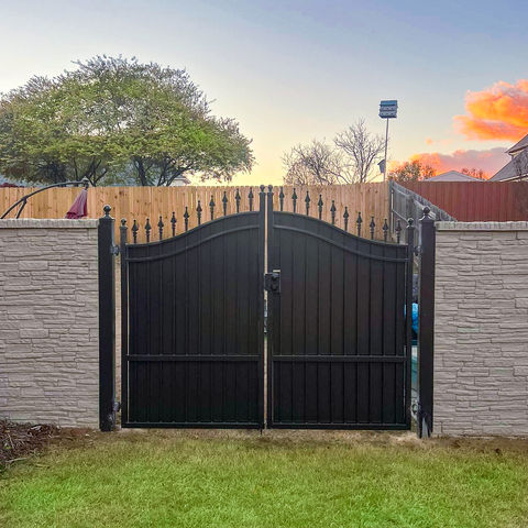Black metal gate between stone pillars, green lawn.