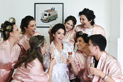 Noiva e madrinhas de robe, brindando de forma descontraída com espumante