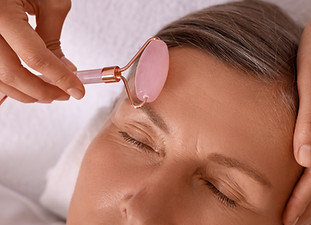 Woman receiving facial massage with rose quartz roller in beauty salon, closeup.jpg