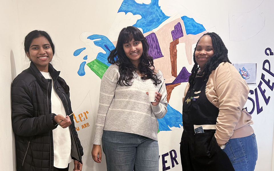 Three people posing in front of a mural they are painting on an interior wall