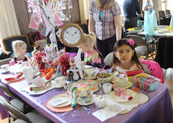 Children at a tea party at a table with Alice in Wonderland decorations