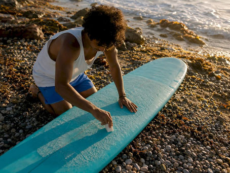 Surfer applying wax to surfboard on beach