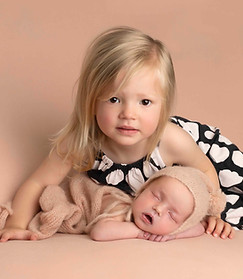 Big sister with her newborn sister photographed on peach background at stork photography, edinburgh newborn photoshoot