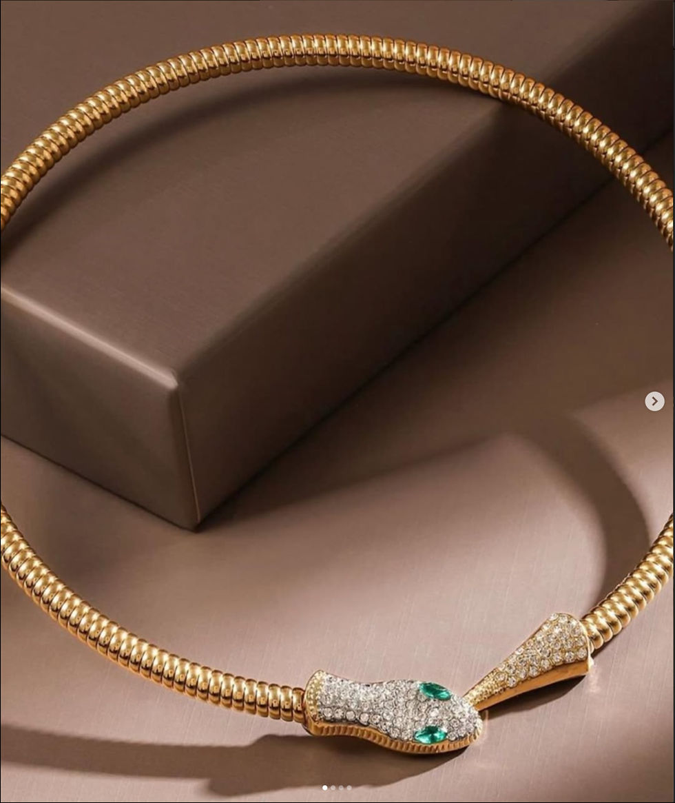 Golden snake necklace with green eyes on a brown surface, stylish design, DHE Studio