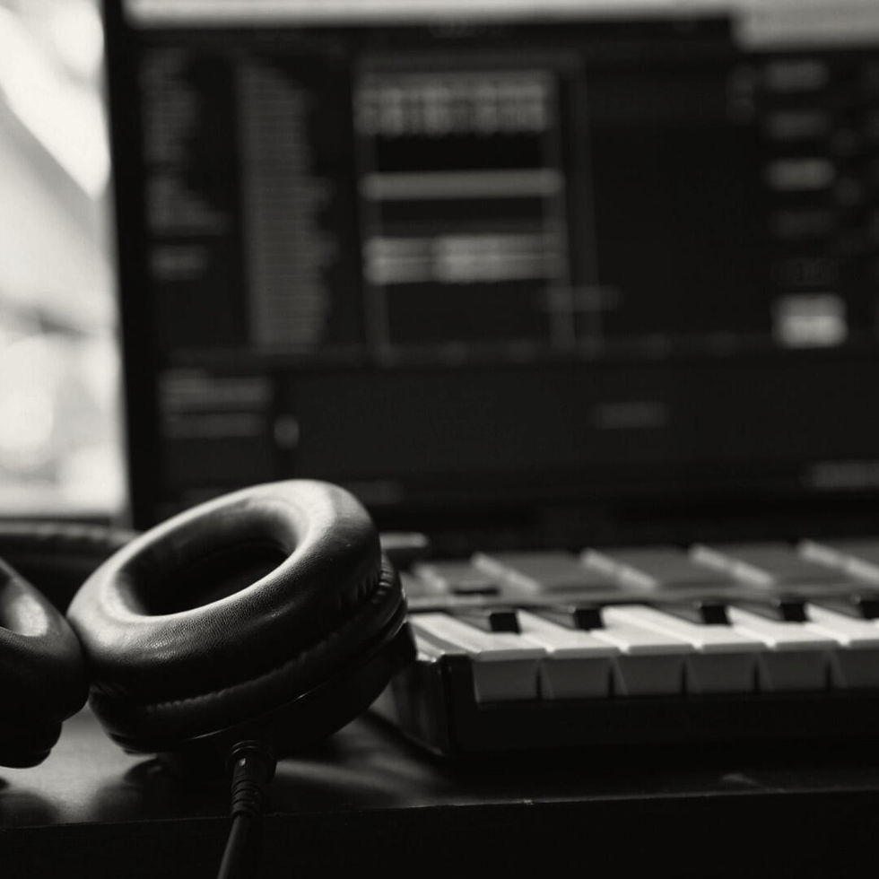 Black headphones resting on a MIDI keyboard, with a blurred computer screen in the background.