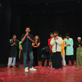 Emcee Agranshu with microphone speaks on stage with group of people applauding.