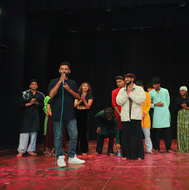 Emcee Agranshu with microphone speaks on stage with group of people applauding.