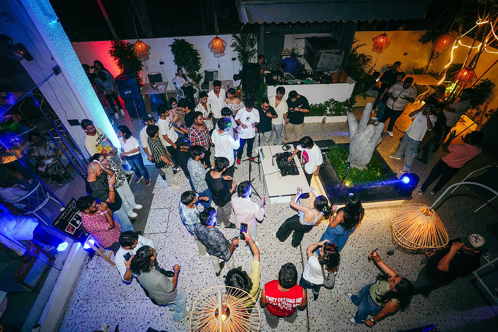 A lively crowd gathers around the DJ at a vibrant outdoor party, enjoying music and colorful lights in an energetic atmosphere.