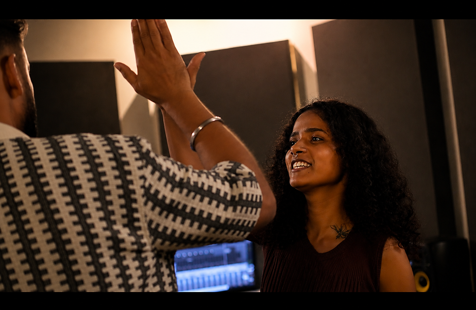 Emcee Agranshu & Stela Crown high-five in a recording studio, smiling under warm light, with acoustic panels in the background.