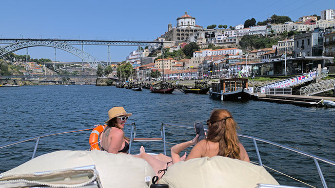 Duas pessoas a relaxar num iate privado com vista para o Porto e a Ponte Luís I ao longo do rio Douro